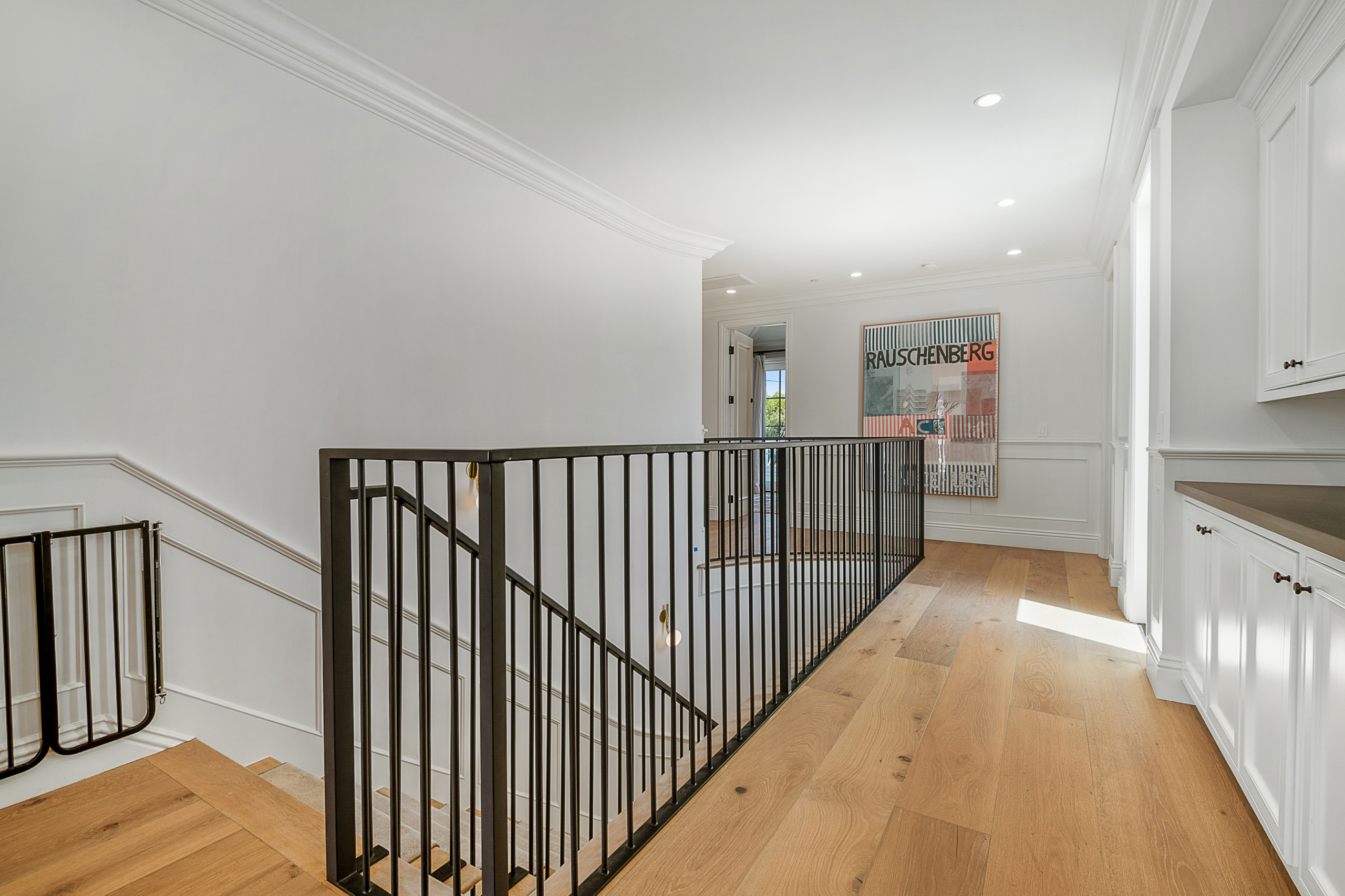 Dark metal staircase with safety gate at top of stairs an long hallway with built-in cabinets