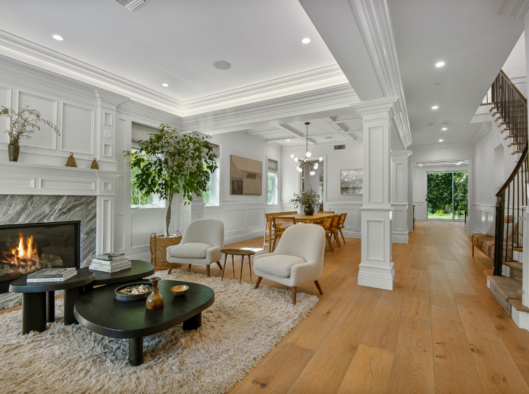 Large living room area with marble fireplace and crowned molding, vaulted ceiling. View through to dining area, staircase and back of inside of the home