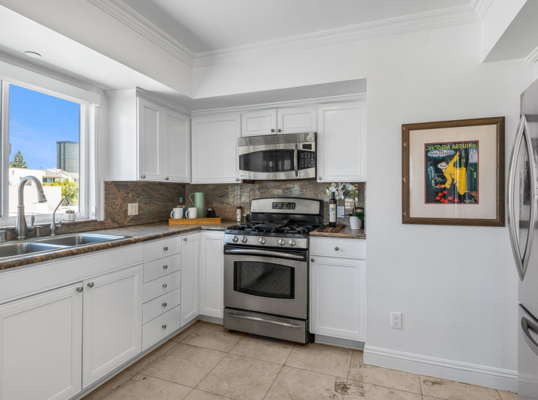 Kitchen with white cabinets, multi-colored granite and stainless appliances.
