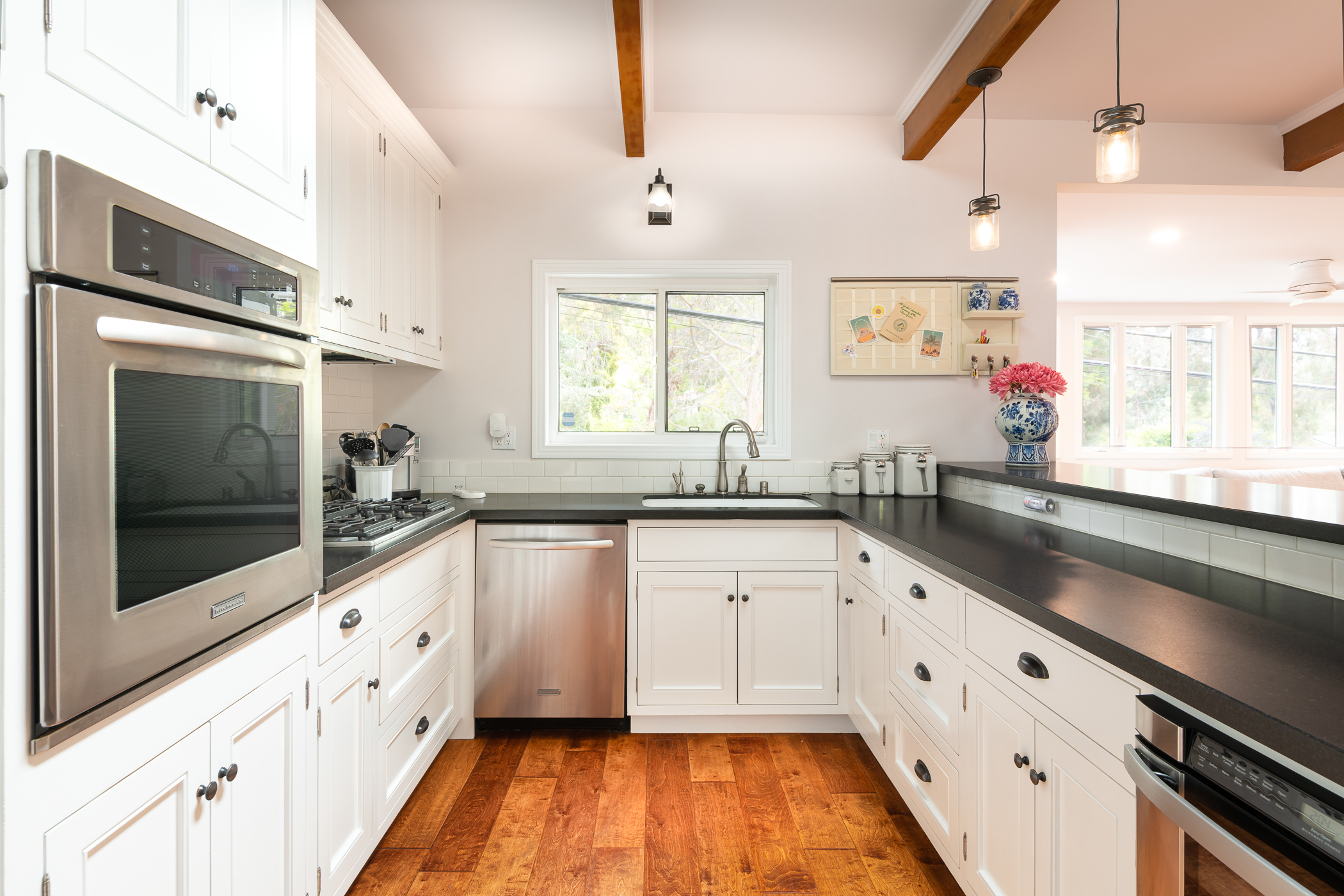 Bright kitchen with wood exposed beams and hand hewn floor and view of black countertops and white cabinets