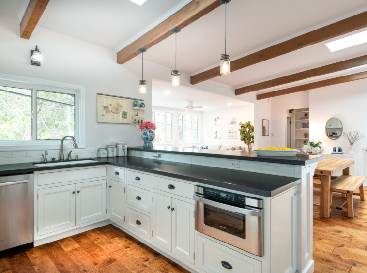 Bright kitchen with wood exposed beams and hand hewn floor and view of black countertops and white cabinets