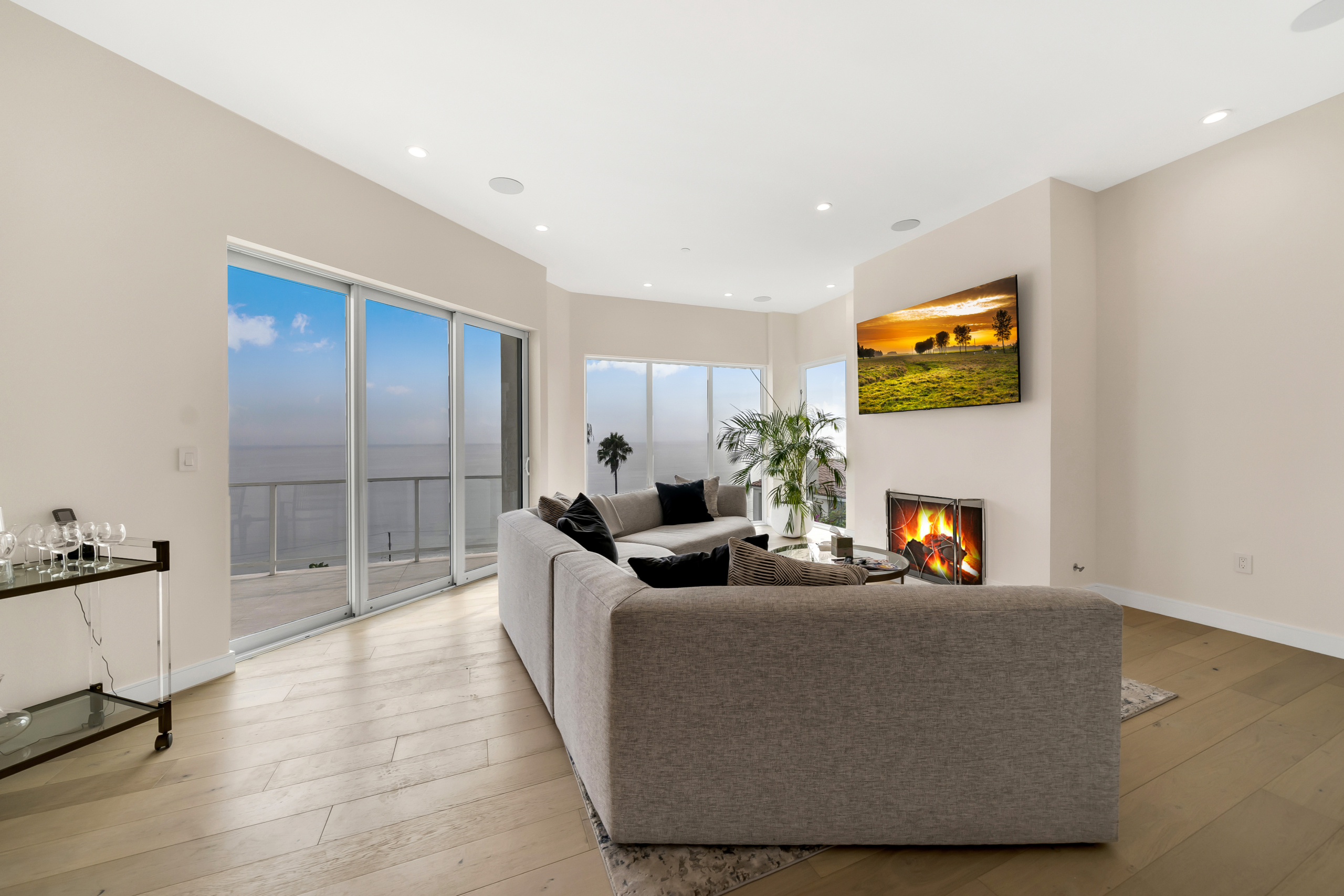 Angled view of living room space and fireplace. A large back of floor-to-ceiling windows and doors looking out to ocean