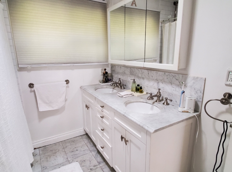 White bathroom with marble countertops. Vanity has two sinks and a large medicine cabinet above