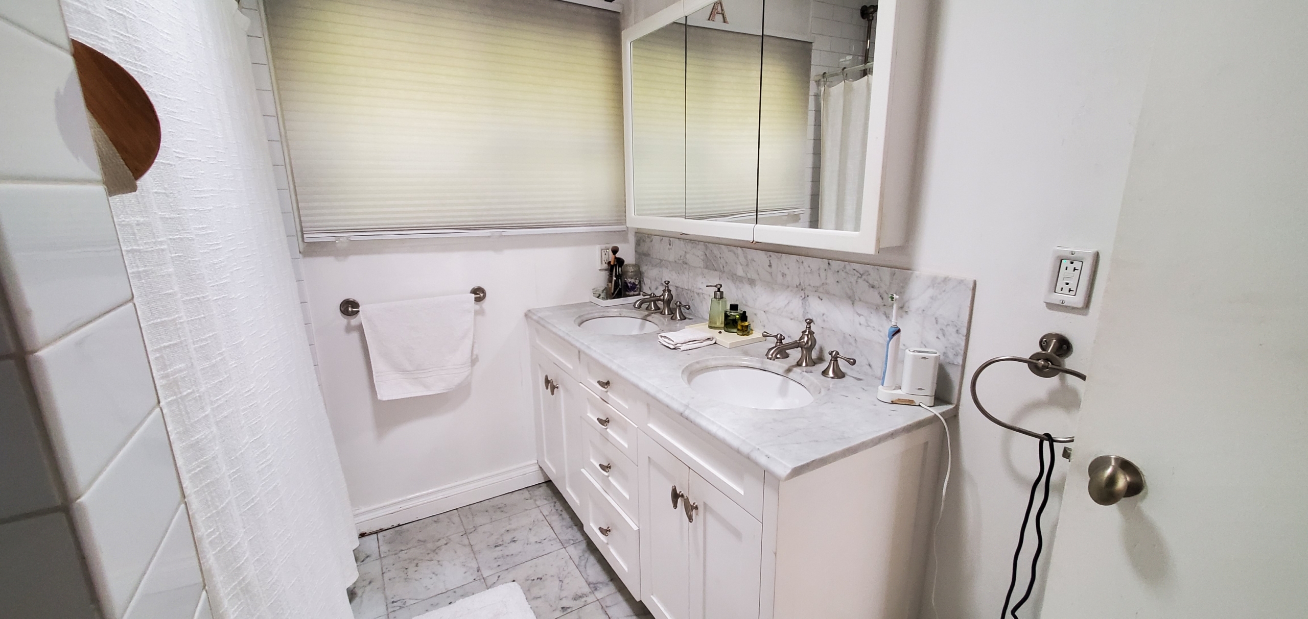 White bathroom with marble countertops. Vanity has two sinks and a large medicine cabinet above