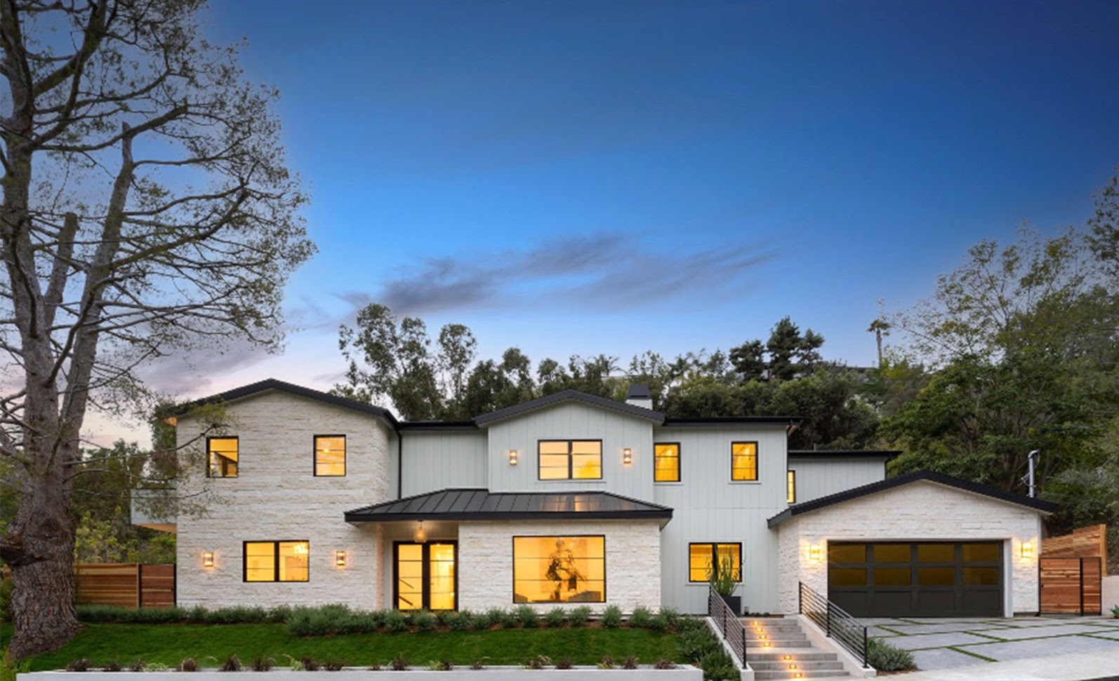 Front of white stone-faced home, concrete driveway and grass lawn area