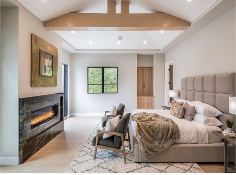 Large bedroom with exposed beams and open ceiling. A large bad sits across from a large in-wall fireplace