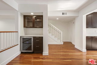 White living room space with hardwood floors showing bar area and wine fridge