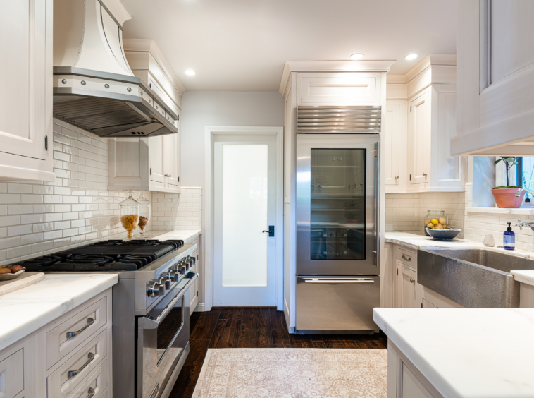 Modern bright, white kitchen with stainless steel appliances, dark hardwood floor and hammered apron sink