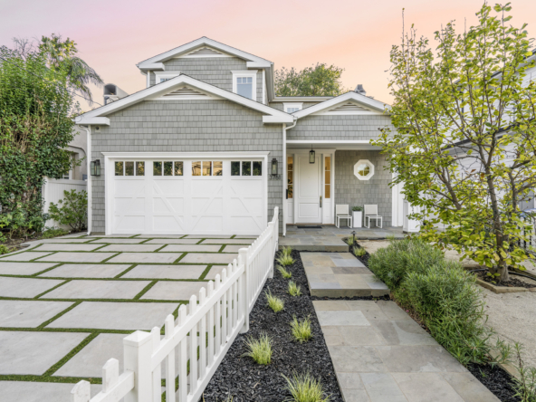 Front of grey shingled home with concrete driveway, picket fence and drought-friendly yard