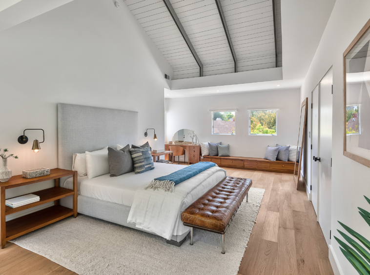 Spacious bright, white bedroom with vaulted ceiling, wood flooring and built-in seating and storage area.